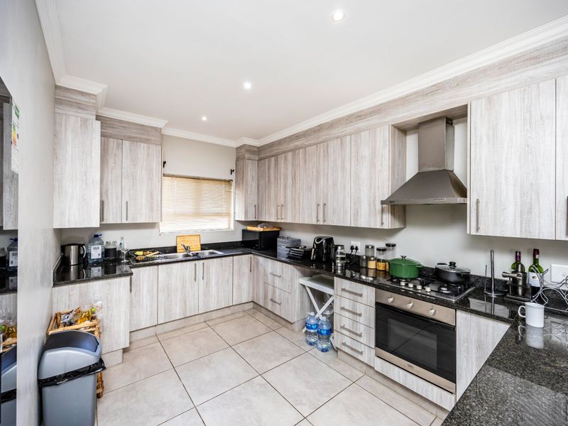 A well-maintained kitchen featuring light wood-grain cabinetry, granite countertops, a built-in oven with gas hob, and a stainless steel extractor fan.