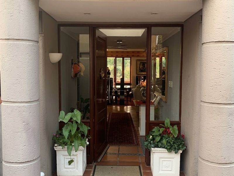 A welcoming entrance featuring terracotta tiled flooring, decorative structural columns, and a timber-framed glass door leading into the home.