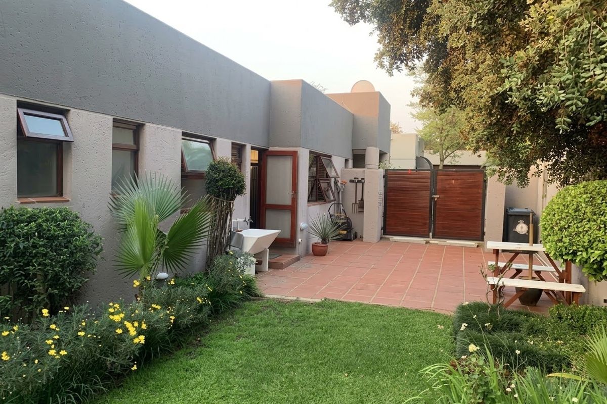 A well-maintained rear exterior featuring a paved patio area, a neat lawn, landscaped garden beds, and a secure timber gate.