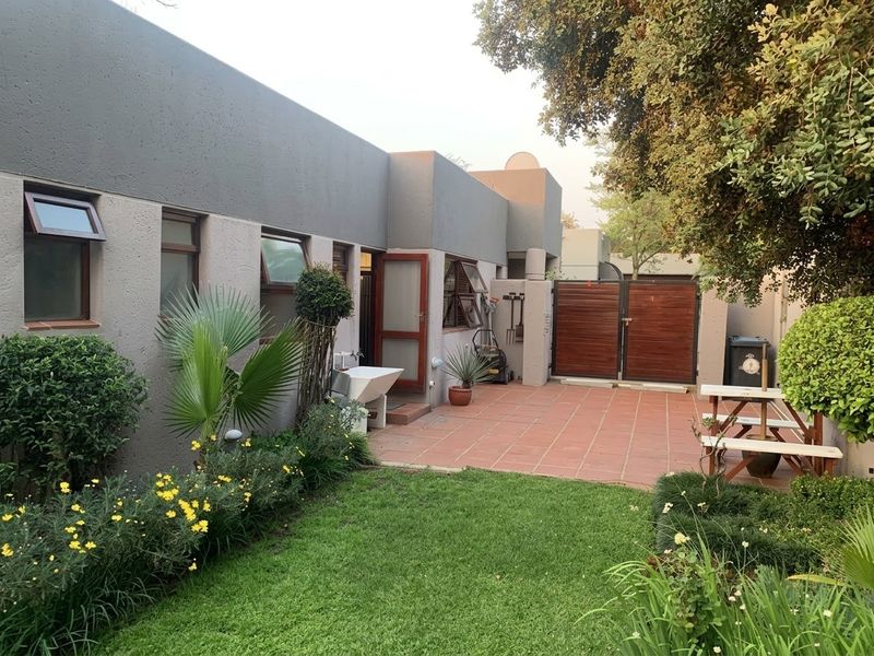 A well-maintained rear exterior featuring a paved patio area, a neat lawn, landscaped garden beds, and a secure timber gate.