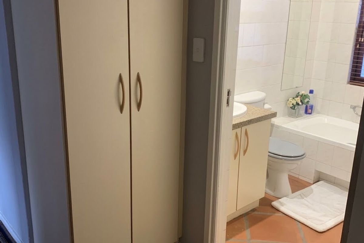 A bathroom featuring a vanity cabinet, toilet, and bathtub with tiled flooring and wall finishes, accessed via a hallway with built-in storage.