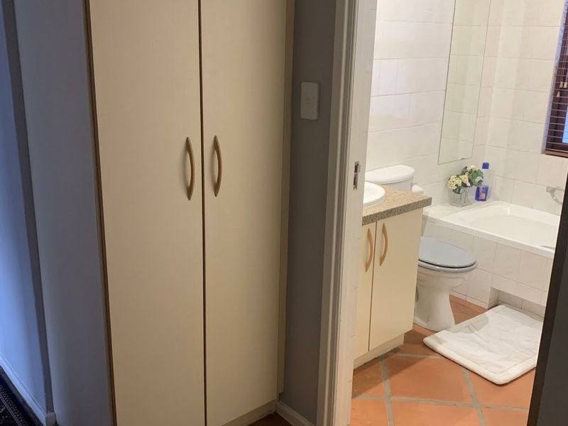 A bathroom featuring a vanity cabinet, toilet, and bathtub with tiled flooring and wall finishes, accessed via a hallway with built-in storage.