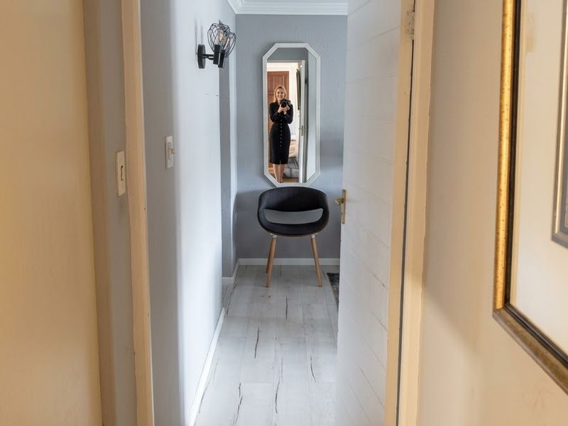 A bright hallway featuring light-toned laminate flooring, crown molding, and a wall-mounted light fixture, providing a clean transition between living spaces.