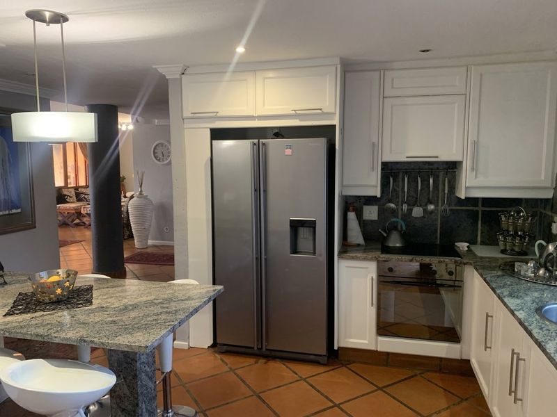 A functional kitchen featuring granite countertops, white cabinetry, built-in oven and hob, and terracotta floor tiles, seamlessly flowing into the adjacent living area.
