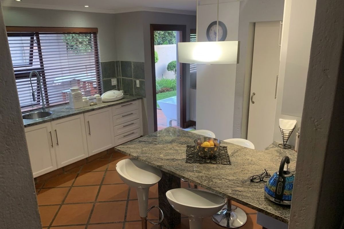 A functional kitchen featuring granite countertops, a central island with breakfast bar seating, tiled flooring, and direct access to the outdoor area.