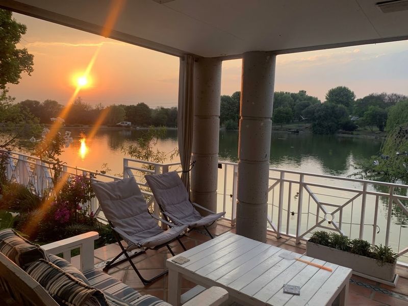 A covered patio area featuring concrete columns and metal railings, offering scenic views of the adjacent lake at sunset.