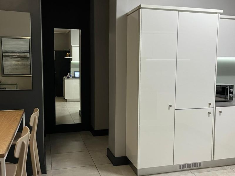 Modern kitchen area featuring sleek white built-in cabinetry, neutral tiled flooring, and clean architectural lines, providing a contemporary and functional living space.