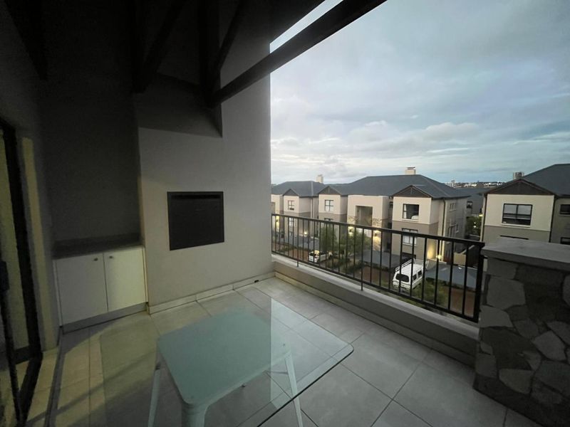 A covered balcony featuring tiled flooring, a built-in braai, and integrated cabinetry, offering an outdoor space with views of the surrounding residential complex.