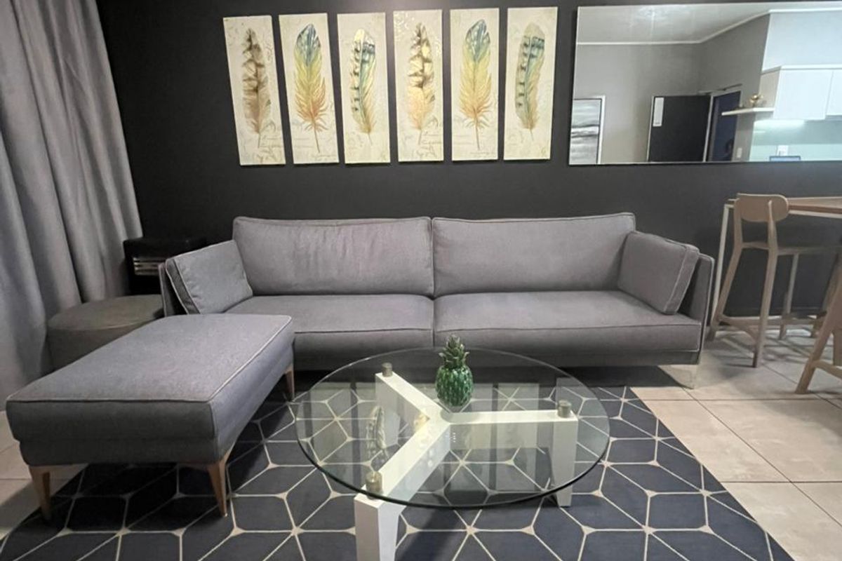 A modern living room featuring large format floor tiles, a dark accent wall, and integrated ceiling lighting, creating a contemporary and comfortable living space.