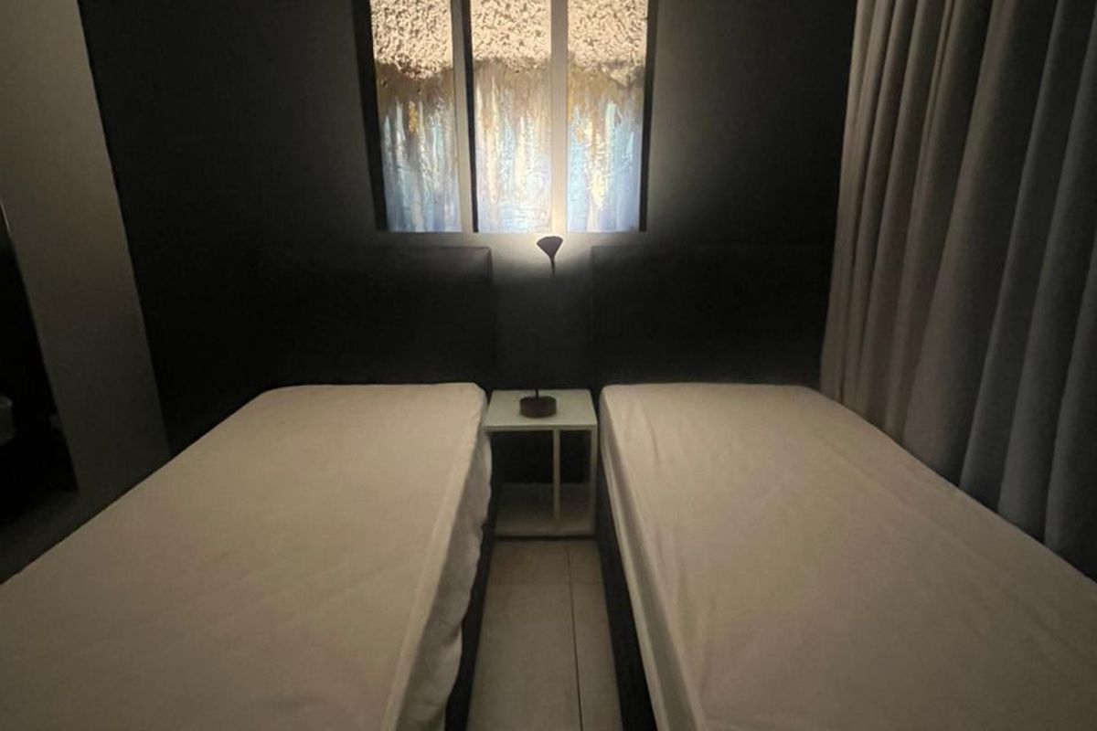 A bedroom featuring tiled flooring and neutral wall finishes, presented with a twin-bed configuration and curtained window treatments.