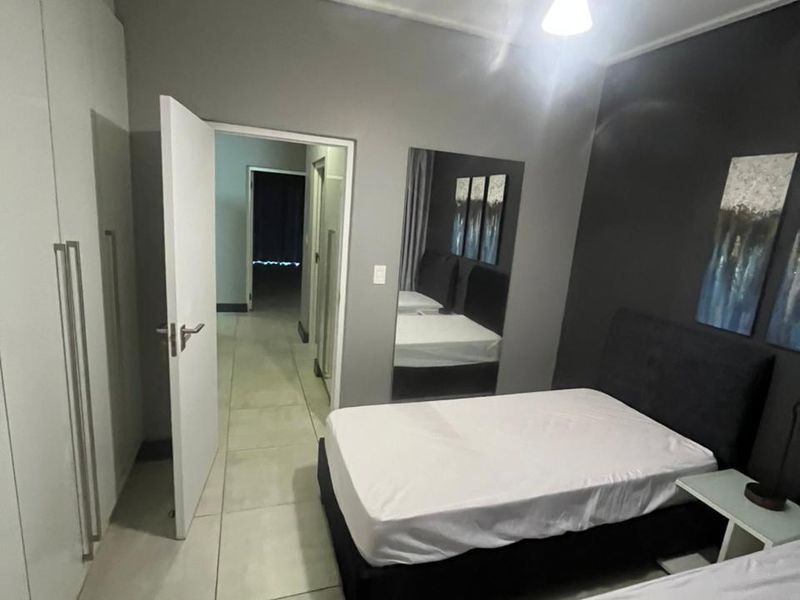 A modern bedroom featuring tiled flooring, built-in cupboards, and a neutral color palette with a dark accent wall.