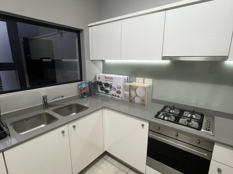 Modern kitchen featuring sleek white cabinetry, stone countertops, stainless steel appliances including a gas hob and oven, and contemporary tiled flooring.