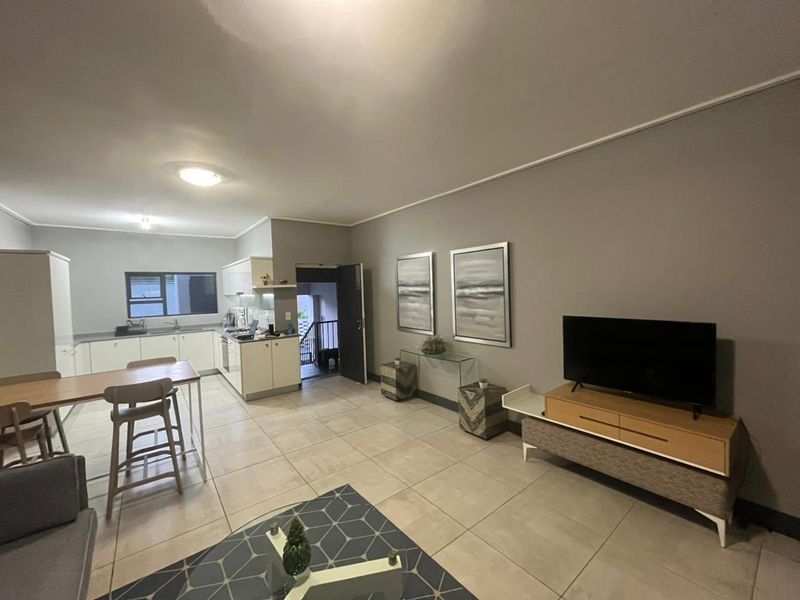 Open-plan living and kitchen area featuring neutral tiled flooring, modern white cabinetry, and integrated kitchen appliances in a well-maintained apartment setting.