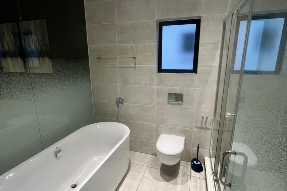 Modern bathroom featuring a sleek freestanding bathtub, wall-mounted toilet, glass-enclosed shower, and neutral floor-to-ceiling tiling with recessed lighting.