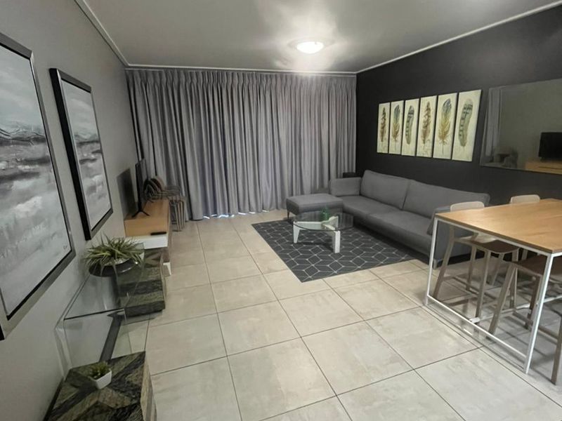 Spacious open-plan living and dining area featuring neutral tiled flooring and large floor-to-ceiling curtains.