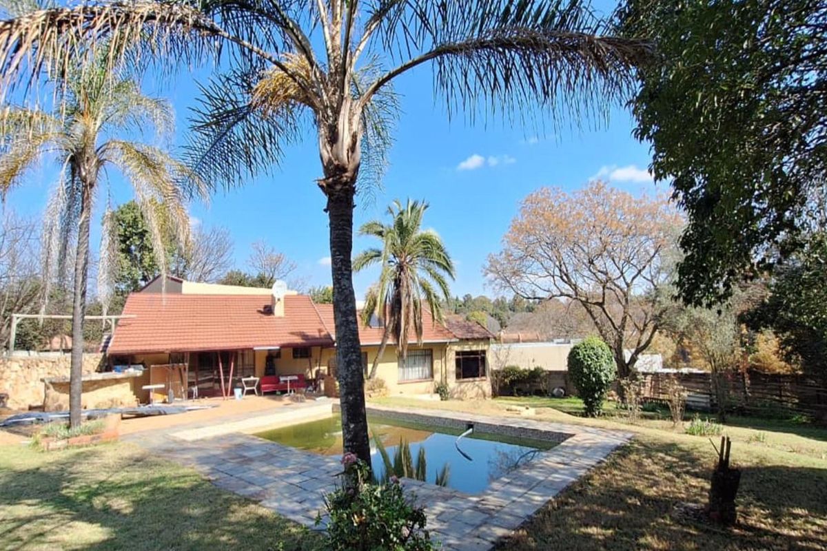 Rear view of the property featuring a swimming pool, stone paved surround, established garden, and a tiled roof house structure.
