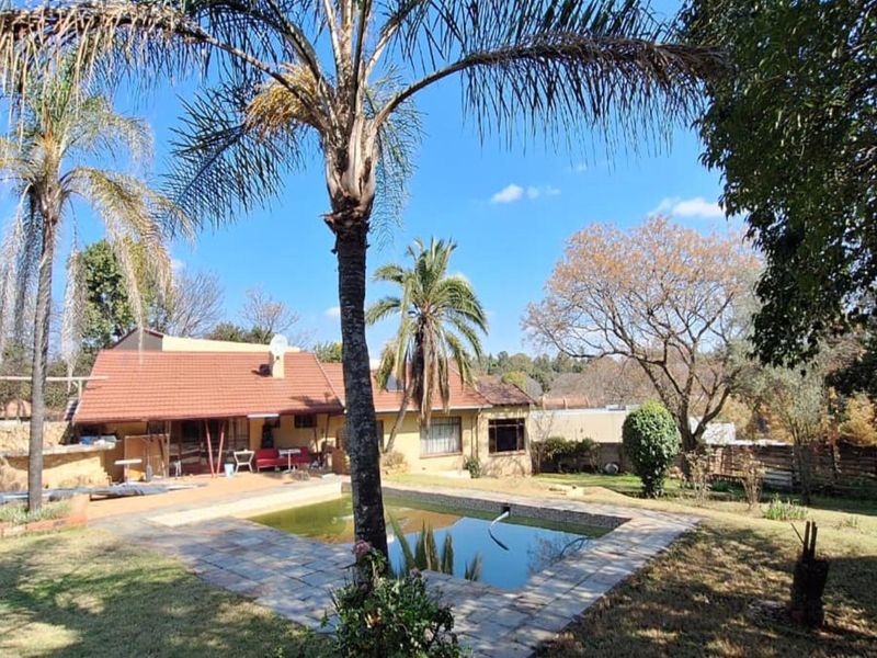 Rear view of the property featuring a swimming pool, stone paved surround, established garden, and a tiled roof house structure.