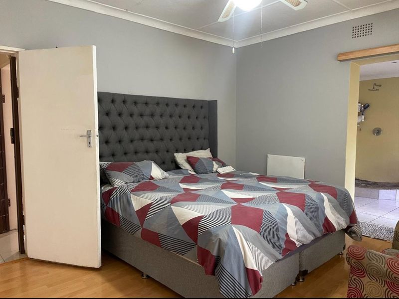 A bedroom featuring laminate flooring, a ceiling fan, and a wall-mounted heater, with an adjoining en-suite bathroom visible.
