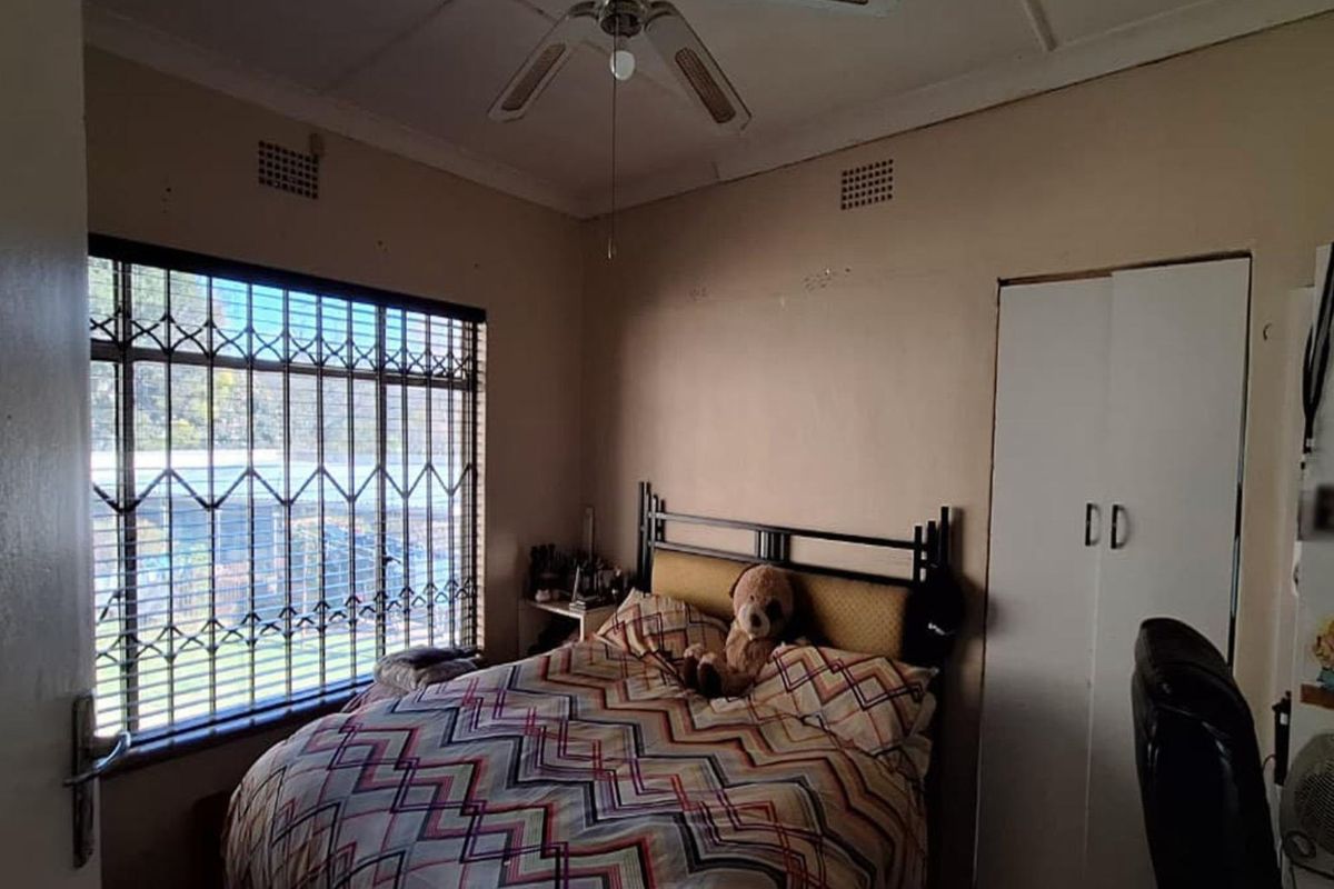 A bedroom featuring a built-in wardrobe, ceiling fan, and security bars on the window. The room requires cosmetic updates to improve its overall condition.