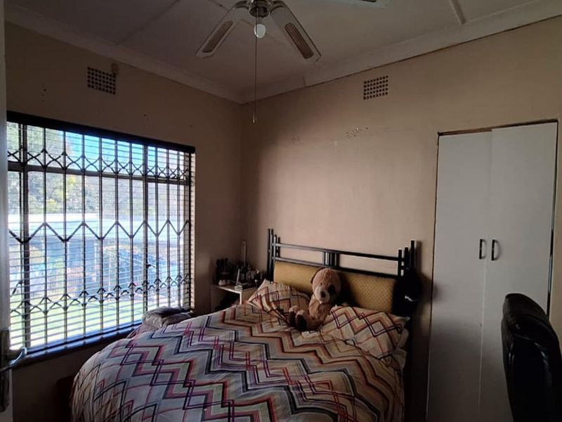 A bedroom featuring a built-in wardrobe, ceiling fan, and security bars on the window. The room requires cosmetic updates to improve its overall condition.