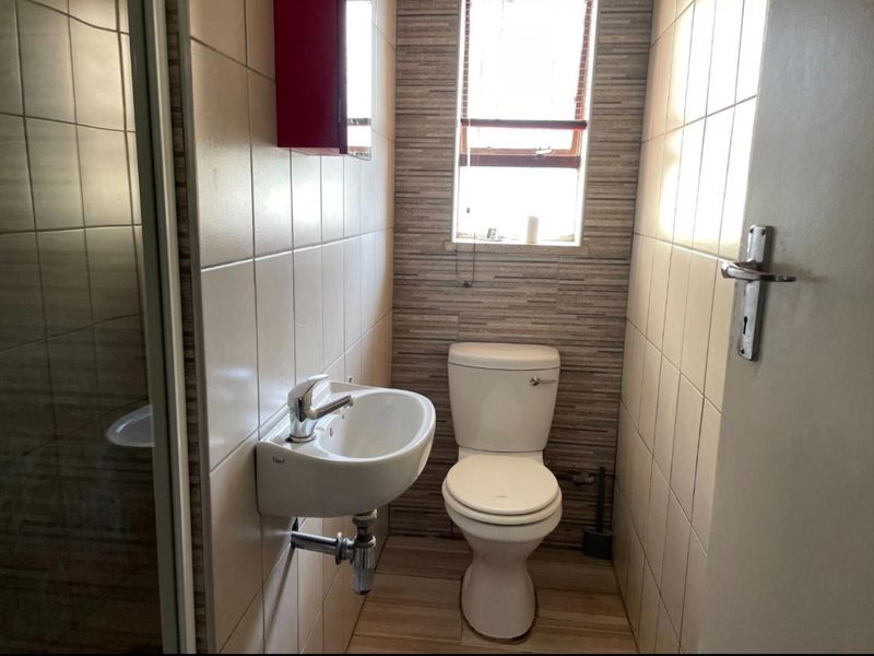 A compact bathroom featuring a wall-mounted basin, toilet, and tiled finishes, providing a functional and clean space.