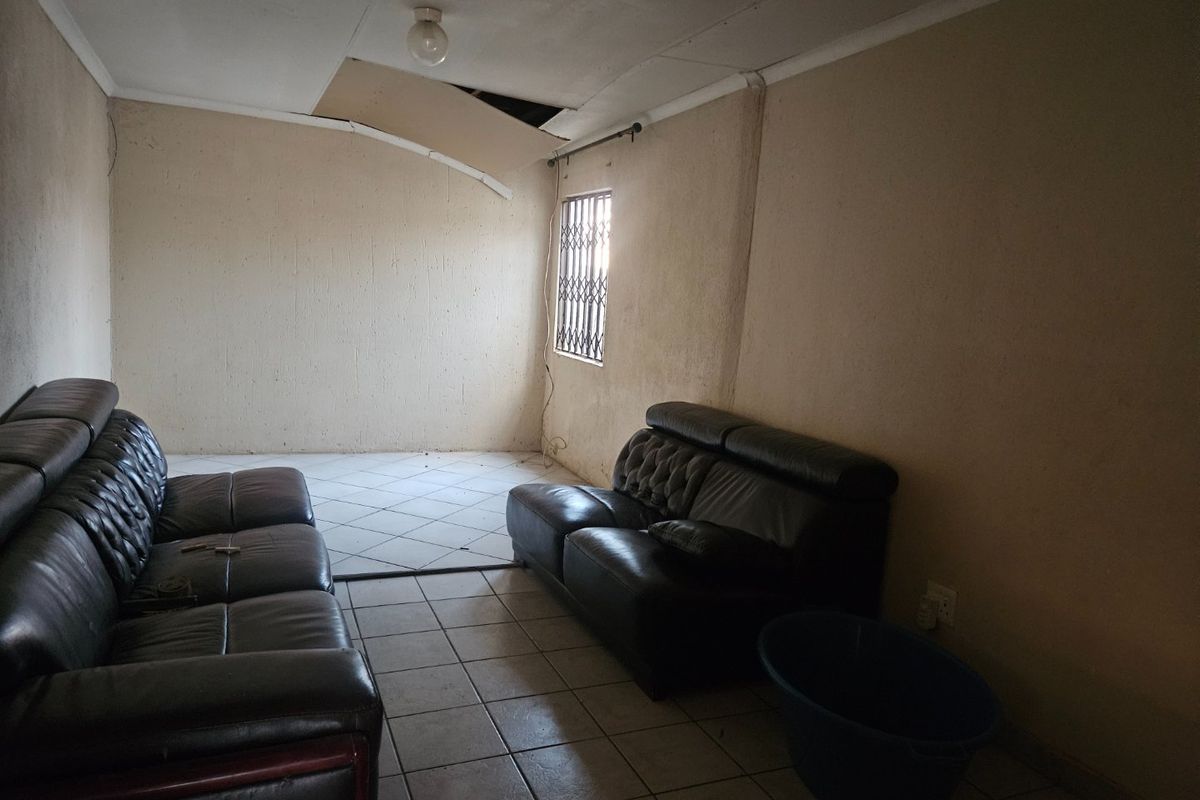 A living room space featuring ceramic floor tiles and a security gate on the window, currently requiring ceiling and wall repairs.