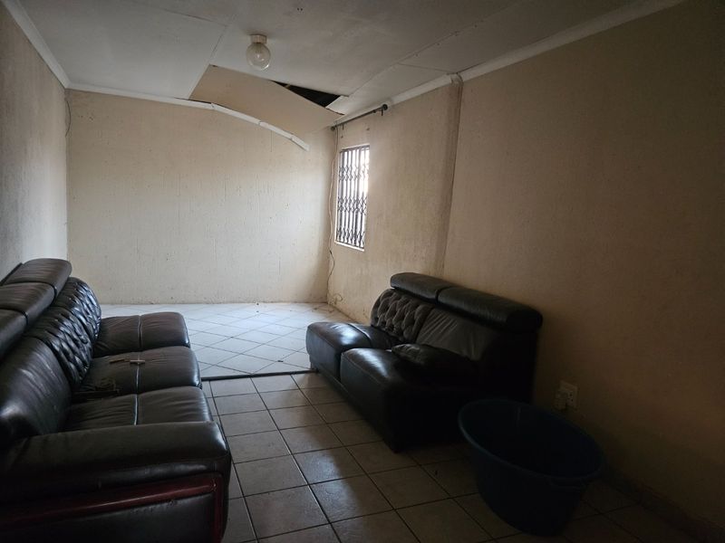 A living room space featuring ceramic floor tiles and a security gate on the window, currently requiring ceiling and wall repairs.