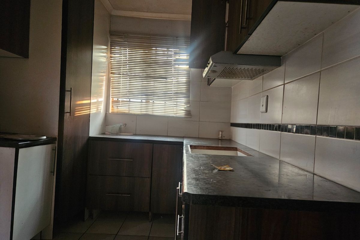 A compact kitchen featuring dark wood-look cabinetry, tiled backsplash, and laminate countertops, currently awaiting a new sink installation and modern updates.