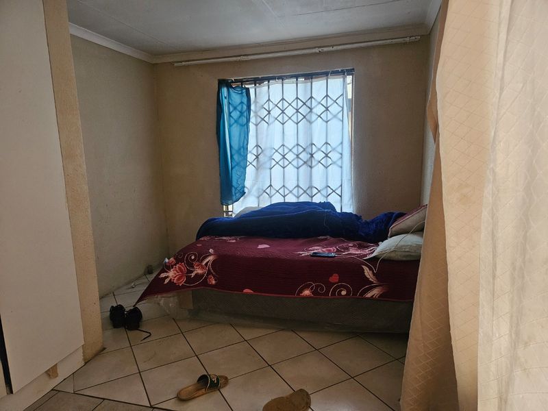 A bedroom featuring tiled flooring, a built-in wardrobe, and a security gate on the window. The room requires cosmetic updates to improve its overall condition.