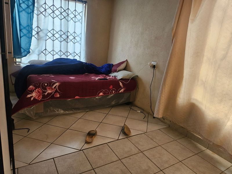 A bedroom featuring tiled flooring and a security gate on the window, requiring cosmetic updates to the wall finishes and flooring.