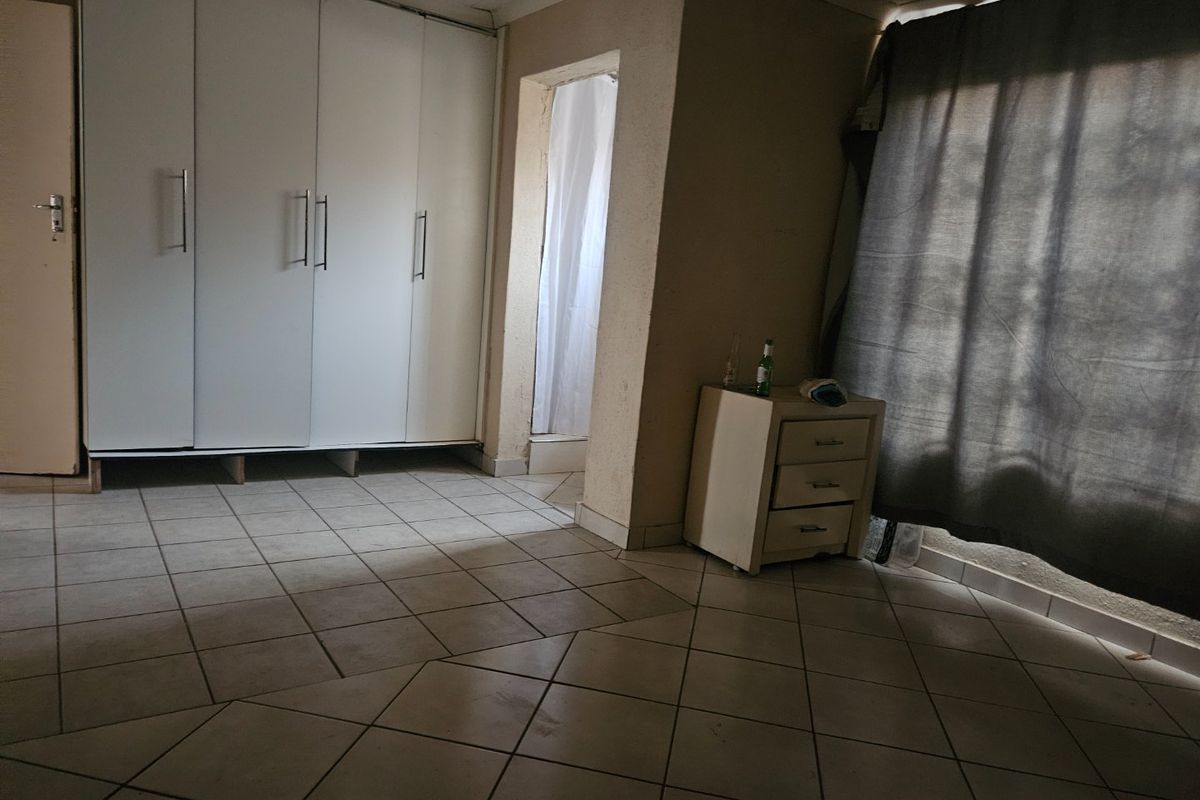 A bedroom featuring built-in cupboards and tiled flooring, with an adjacent en-suite area visible.