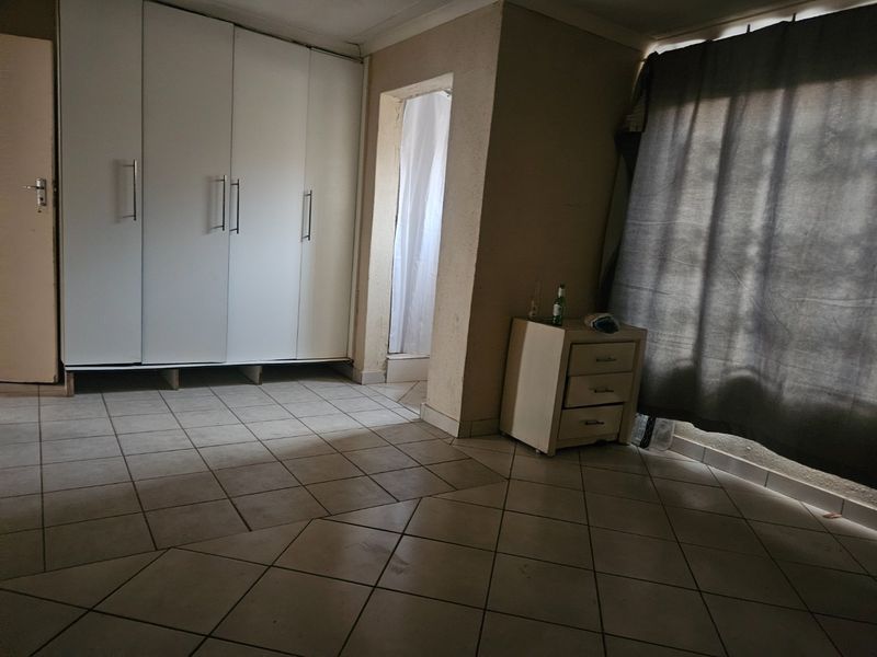 A bedroom featuring built-in cupboards and tiled flooring, with an adjacent en-suite area visible.
