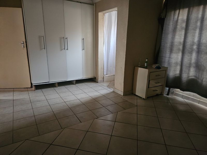 Bedroom featuring built-in cupboards and tiled flooring, with an adjacent doorway leading to an en-suite area.