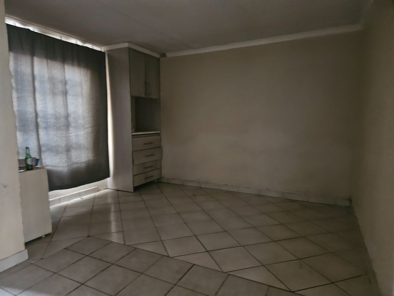 An empty living area featuring tiled flooring, coved ceilings, and built-in cabinetry, offering a blank canvas for renovation and interior design.