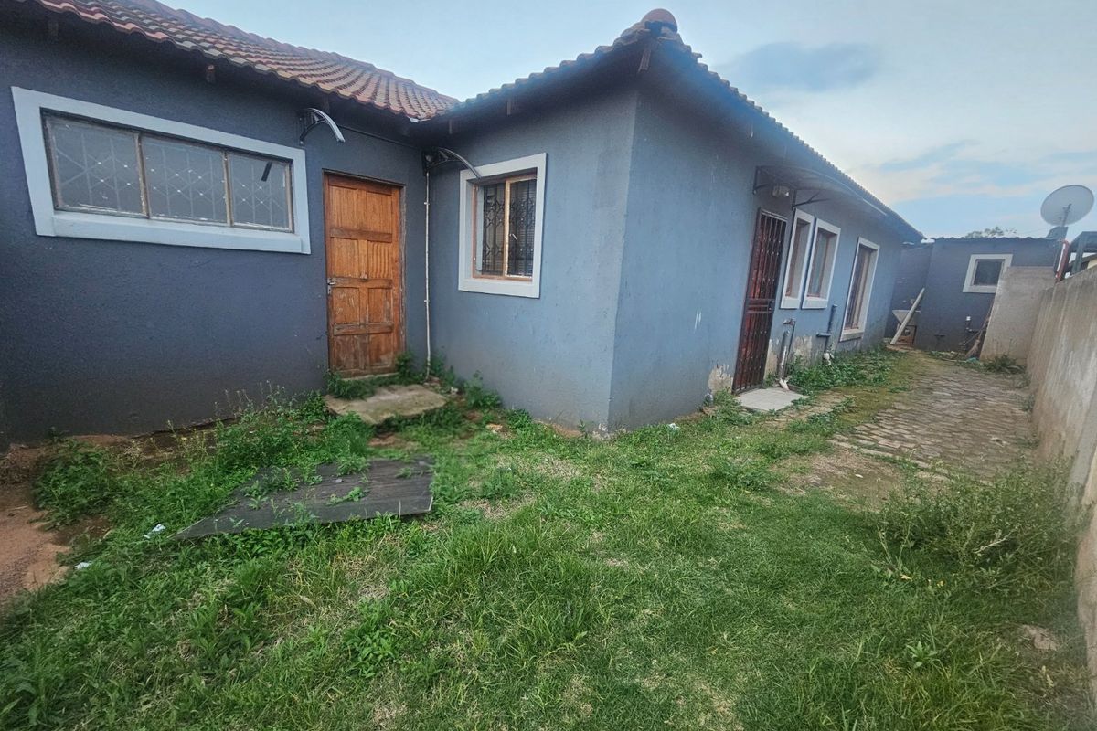 Rear exterior view of the property featuring a tiled roof, security gates, and a paved walkway, requiring maintenance to the exterior walls and garden.