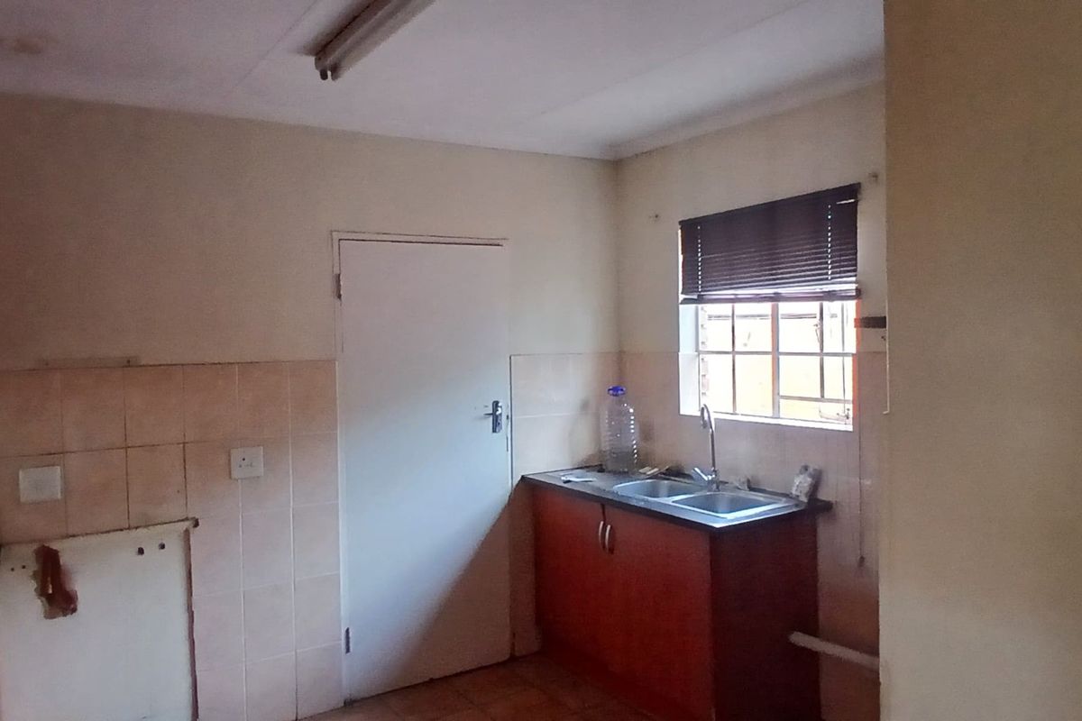 A dated kitchen featuring basic cabinetry, a double sink, and tiled splashbacks, requiring renovation to modernize the space.