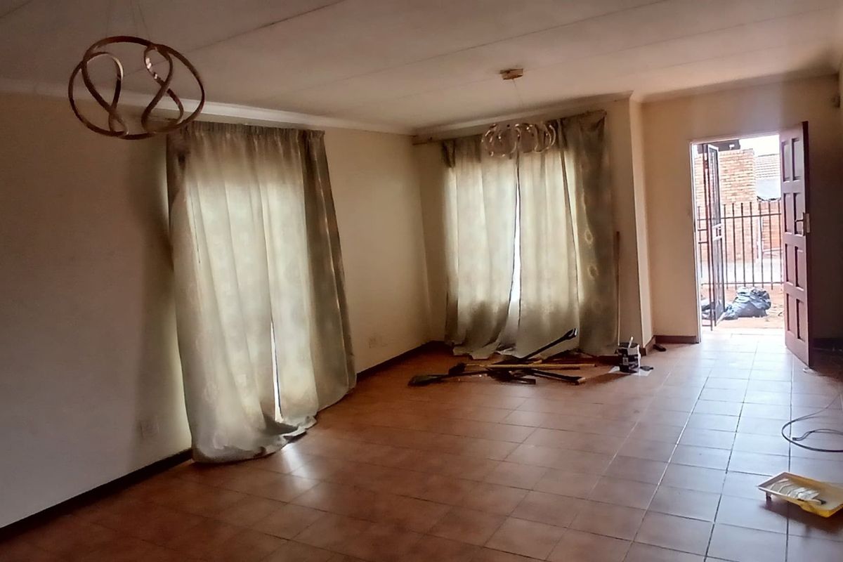 An empty living room featuring tiled flooring, ceiling coving, and direct access to an outdoor area through a security gate.