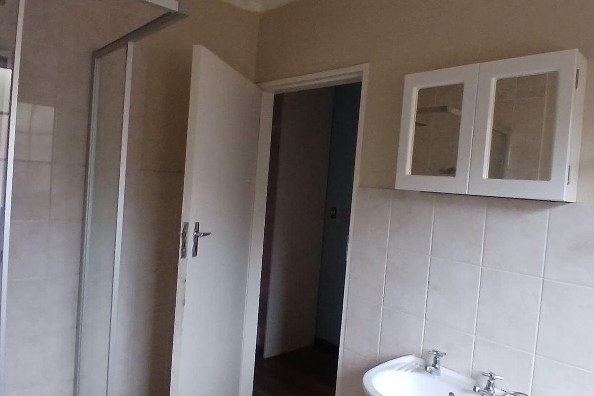 A functional bathroom featuring a shower enclosure, pedestal basin, and wall-mounted storage cabinet with neutral wall tiling.