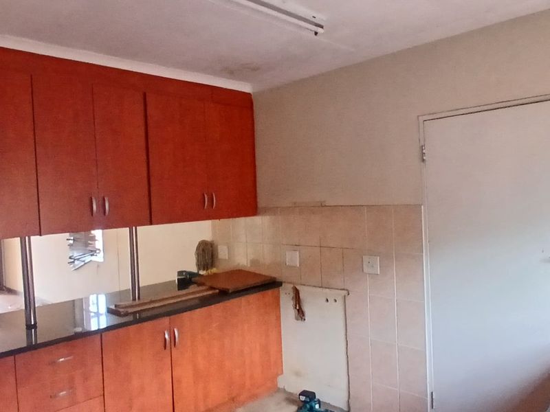A dated kitchen featuring wood-finish cabinetry, granite countertops, and a tiled backsplash, currently vacant and ready for renovation.