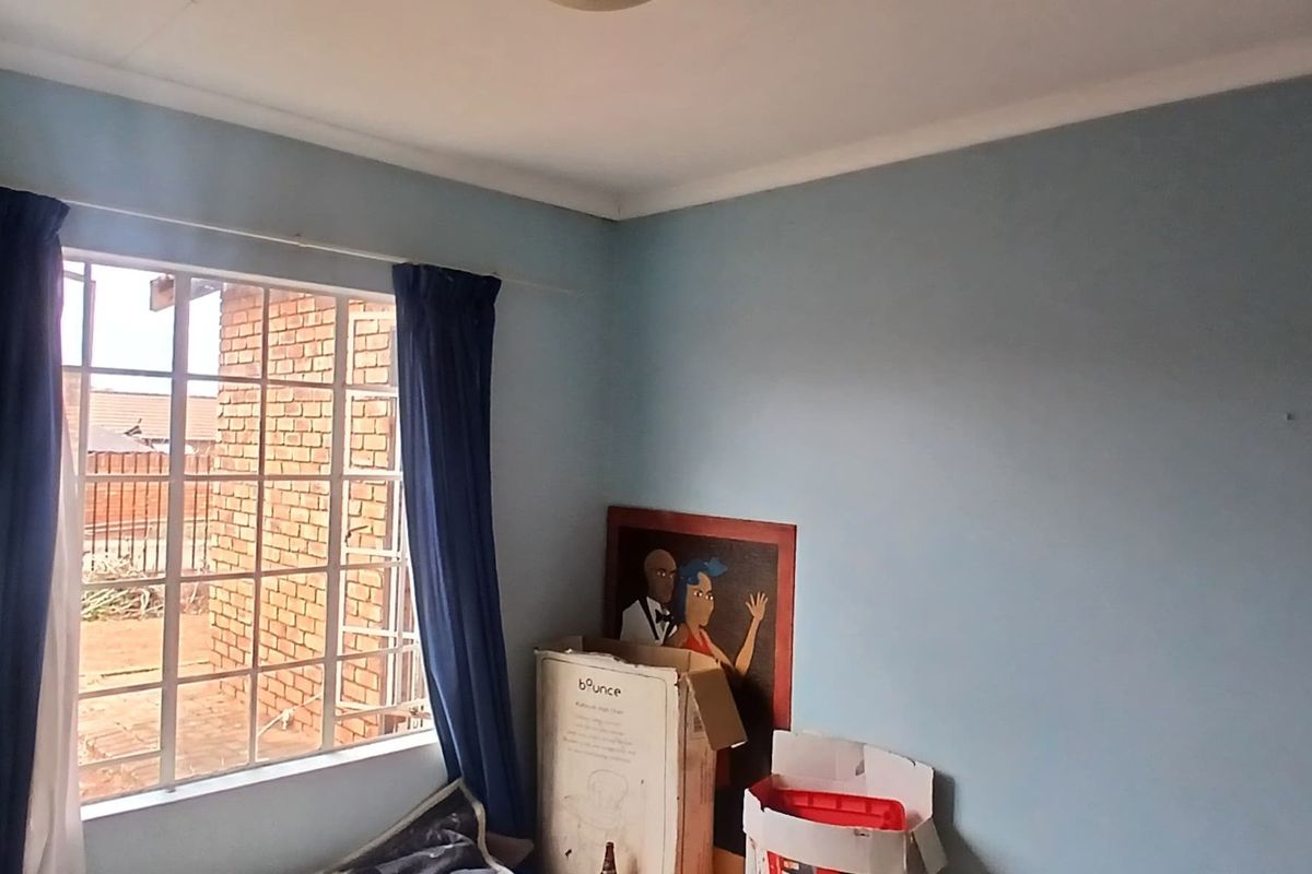 A simple bedroom featuring a window with security burglar bars and standard ceiling cornice, offering a blank canvas for potential interior updates.