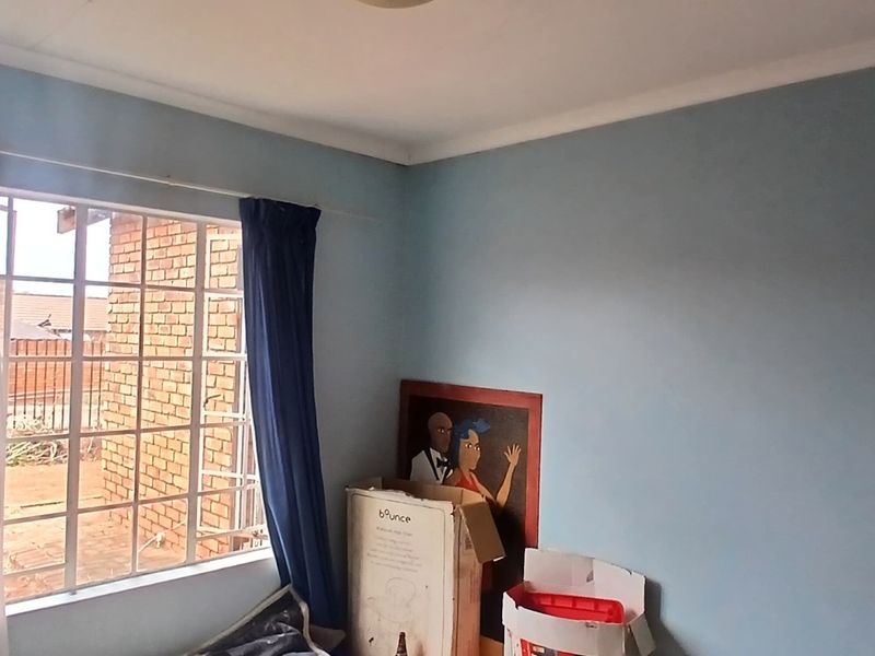 A simple bedroom featuring a window with security burglar bars and standard ceiling cornice, offering a blank canvas for potential interior updates.