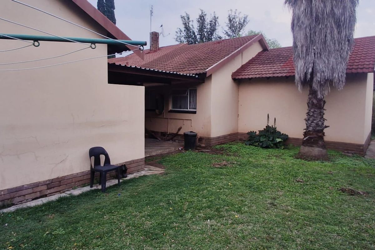 Rear view of the property featuring a tiled roof, concrete patio area, and a spacious garden with a precast boundary wall.