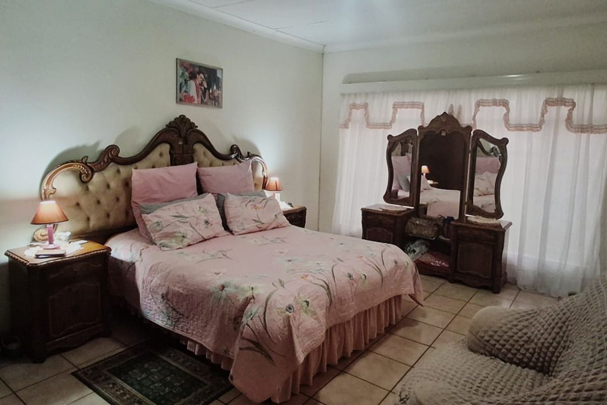 A spacious bedroom featuring tiled flooring and a large window with a curtain rail, offering a neutral base for potential interior updates.