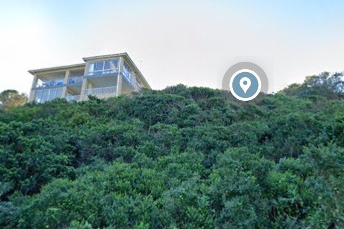 A view of a sloped residential plot covered in dense natural vegetation, with a multi-story building visible at the top of the incline.