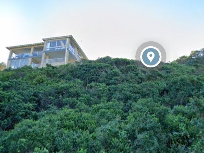 A view of a sloped residential plot covered in dense natural vegetation, with a multi-story building visible at the top of the incline.