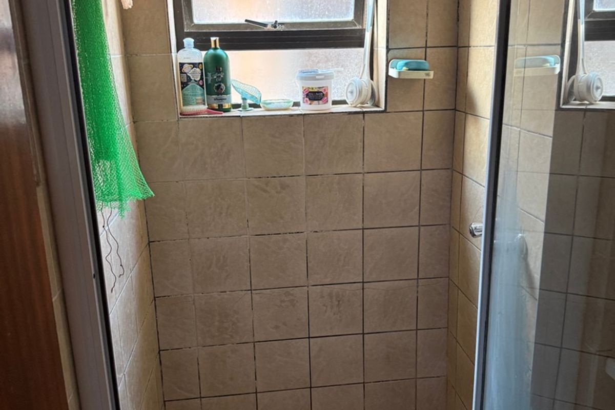 A compact shower stall featuring tiled walls and flooring with a built-in shower head and window for natural light.