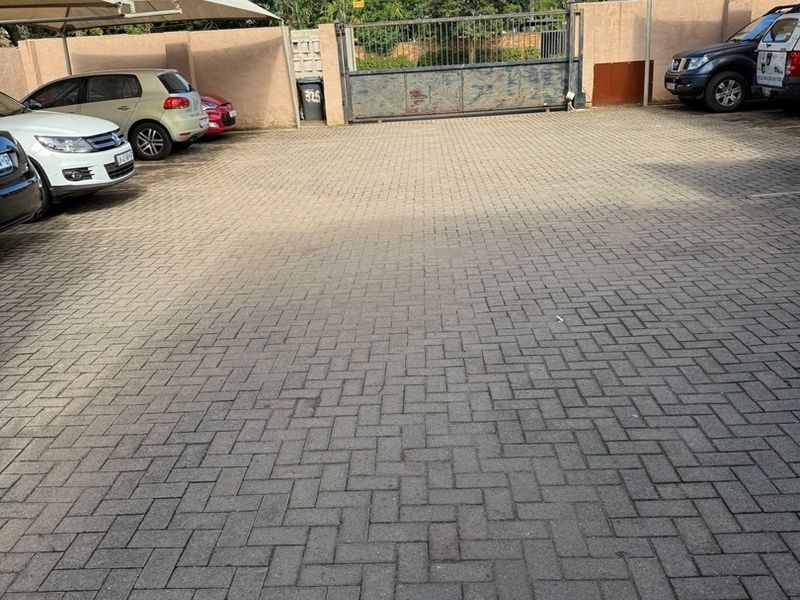 A paved parking area featuring shade cloth carports, perimeter walling, and a secure metal entrance gate.