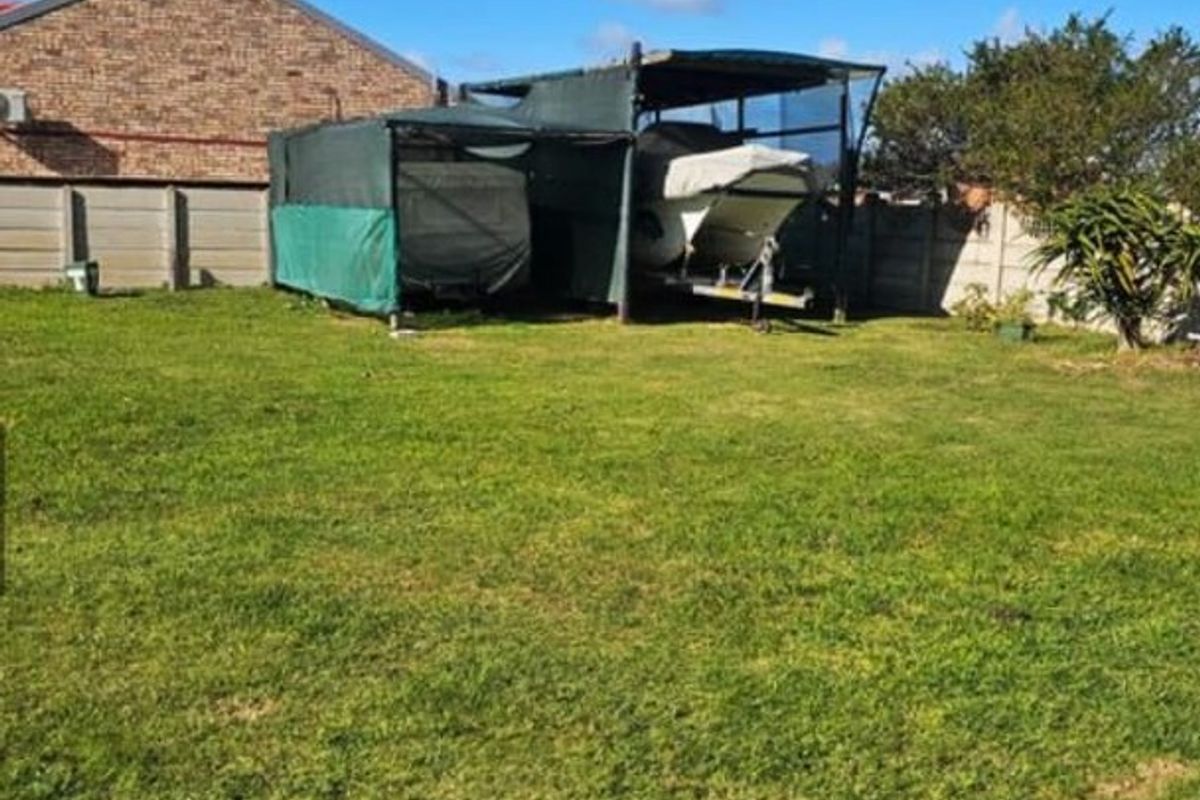 A spacious residential backyard featuring a grass lawn, perimeter precast concrete walling, and a temporary shade cloth structure for vehicle or boat storage.