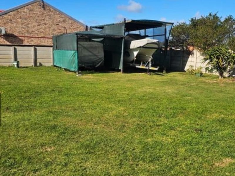 A spacious residential backyard featuring a grass lawn, perimeter precast concrete walling, and a temporary shade cloth structure for vehicle or boat storage.