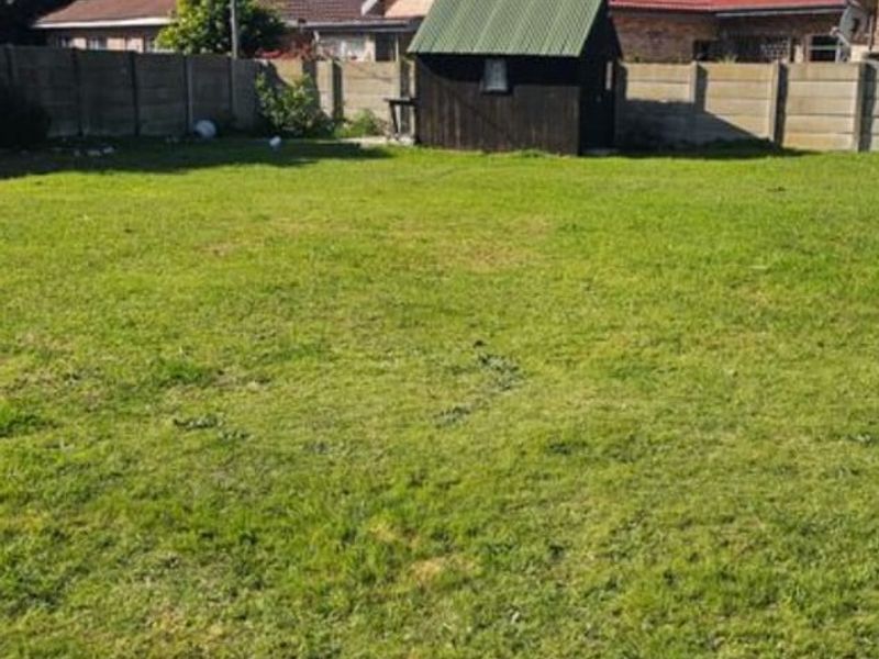 A spacious residential backyard featuring a level lawn, enclosed by precast concrete boundary walls and including a small wooden storage shed.